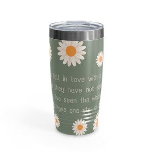 May include: A green travel tumbler with a silver lid, adorned with white daisies with orange centers. The tumbler features white text that reads "fall in love with a, they have not see, I've seen the whole, have one star in".