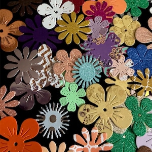 Peut inclure: Une collection de découpes de fleurs en papier assorties de formes, tailles et couleurs variées, notamment orange, vert, violet, doré et bleu. Les fleurs présentent des textures diverses, dont des paillettes, des finitions métalliques et des motifs imprimés.