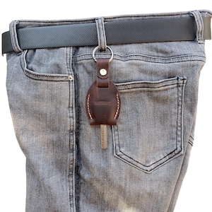 May include: A brown leather key chain with the word "MEEBOY" embossed on it. The key chain is attached to a pair of jeans with a belt.