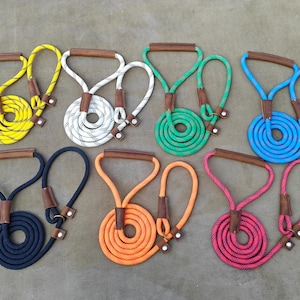 Könnte beinhalten: Eine Sammlung von acht Hundeleinen in verschiedenen Farben, darunter Gelb, Weiß, Grün, Blau, Marine, Orange und Pink. Jede Leine hat ein Design aus gewickeltem Seil mit einem braunen Ledergriff und Akzenten.