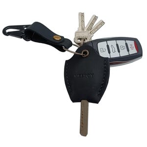 May include: A black leather key cover with the word "MEERBOY" embossed on it. The cover is attached to a black leather key chain with a metal clip and a silver key ring. A car key fob and several keys are attached to the ring.
