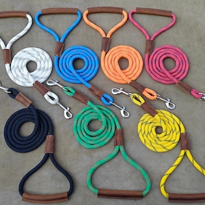May include: A selection of dog leads in a variety of colours: white, blue, orange, pink, black, green, and yellow. Each lead has a rope design, a leather handle, and a metal clasp for secure attachment.