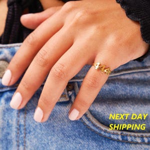 May include: Gold ring with the number 444 on it. The ring is on a person's finger.