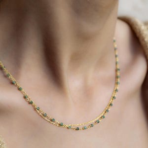 May include: A delicate gold chain necklace with small green gemstone beads. The necklace is layered, creating a subtle and elegant look.
