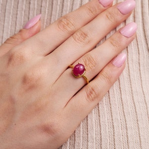 May include: A gold ring with a large oval-shaped ruby gemstone set in a prong setting.