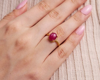 May include: A gold ring with a large oval-shaped ruby gemstone set in a prong setting.