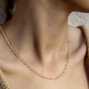 May include: A delicate gold chain necklace with small, clear beads. The necklace is layered, creating a subtle and elegant look.