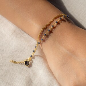 May include: A gold chain bracelet with small blue beads and a larger blue gemstone charm.