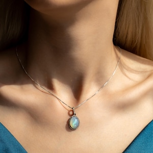 May include: A silver chain necklace with a pendant featuring a light blue oval opal surrounded by a halo of small diamonds.