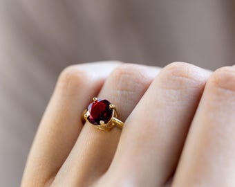May include: A gold ring with a large, round, red gemstone.
