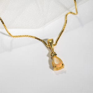 May include: A gold chain necklace with a teardrop-shaped opal pendant.