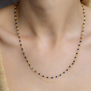 May include: A gold chain necklace with two strands of small blue beads. The necklace is layered and has a delicate look.