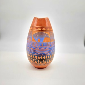 Puede incluir: Un jarrón de cerámica pintado a mano con un diseño geométrico marrón, azul y naranja. El jarrón tiene forma de lágrima y un acabado liso y brillante.