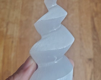 May include: White selenite crystal carved into a spiral shape. The crystal is smooth and polished, with a translucent appearance.