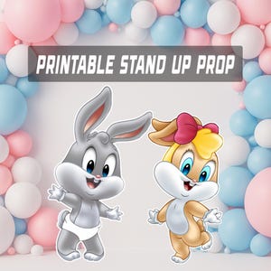 May include: Printable stand-up prop featuring cartoon characters. A gray bunny wearing a diaper and a tan bunny with a pink bow are shown. The background includes pink, white, and blue balloons, creating a festive atmosphere.
