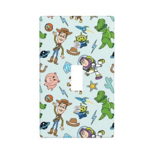 May include: A rectangular light blue light switch cover plate featuring a repeating pattern of cartoon characters including a cowboy, a space ranger, a green dinosaur, a pig, and an alien, interspersed with rockets, stars, and lightning bolts.