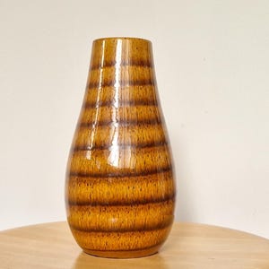 May include: A brown ceramic vase with a ribbed design. The vase has a glossy finish and a rounded shape.