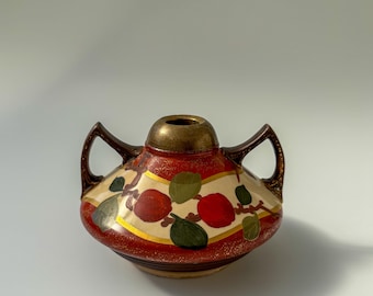 Peut inclure: Un petit vase en céramique rouge et or avec deux anses et un motif peint de fruits rouges et de feuilles vertes.
