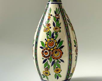 May include: A white ceramic vase with a floral design in shades of blue, green, yellow, and orange. The vase has a rounded body and a narrow neck.