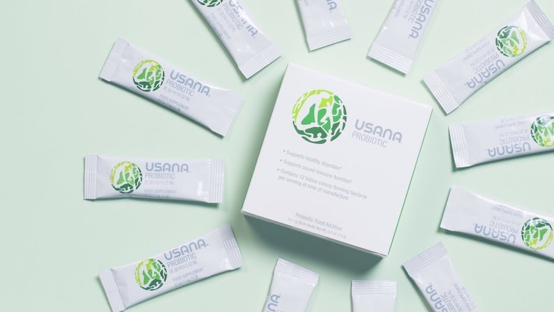 May include: A white box with green text and a green logo that says "USANA PROBIOTIC" on it. The box is surrounded by 10 white packets with green text and logos that say "USANA PROBIOTIC".