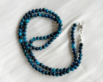Puede incluir: Un collar de cuentas de ojo de tigre azul con cierre de plata. El collar está hecho de cuentas redondas y mide aproximadamente 45 cm de largo.