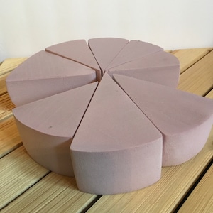May include: A set of eight light purple foam cake slices arranged in a circle on a wooden surface.