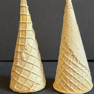 May include: Two white waffle cone ice cream cones. The cones are made of a light brown waffle material and have a slightly textured surface.