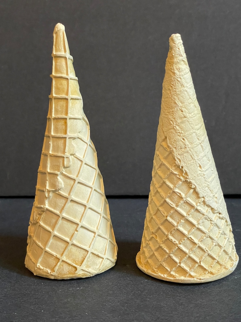 May include: Two white waffle cone ice cream cones. The cones are made of a light brown waffle material and have a slightly textured surface.