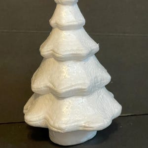 May include: A white polystyrene Christmas tree with a textured surface. The tree is approximately 15 cm tall and has a rounded base.