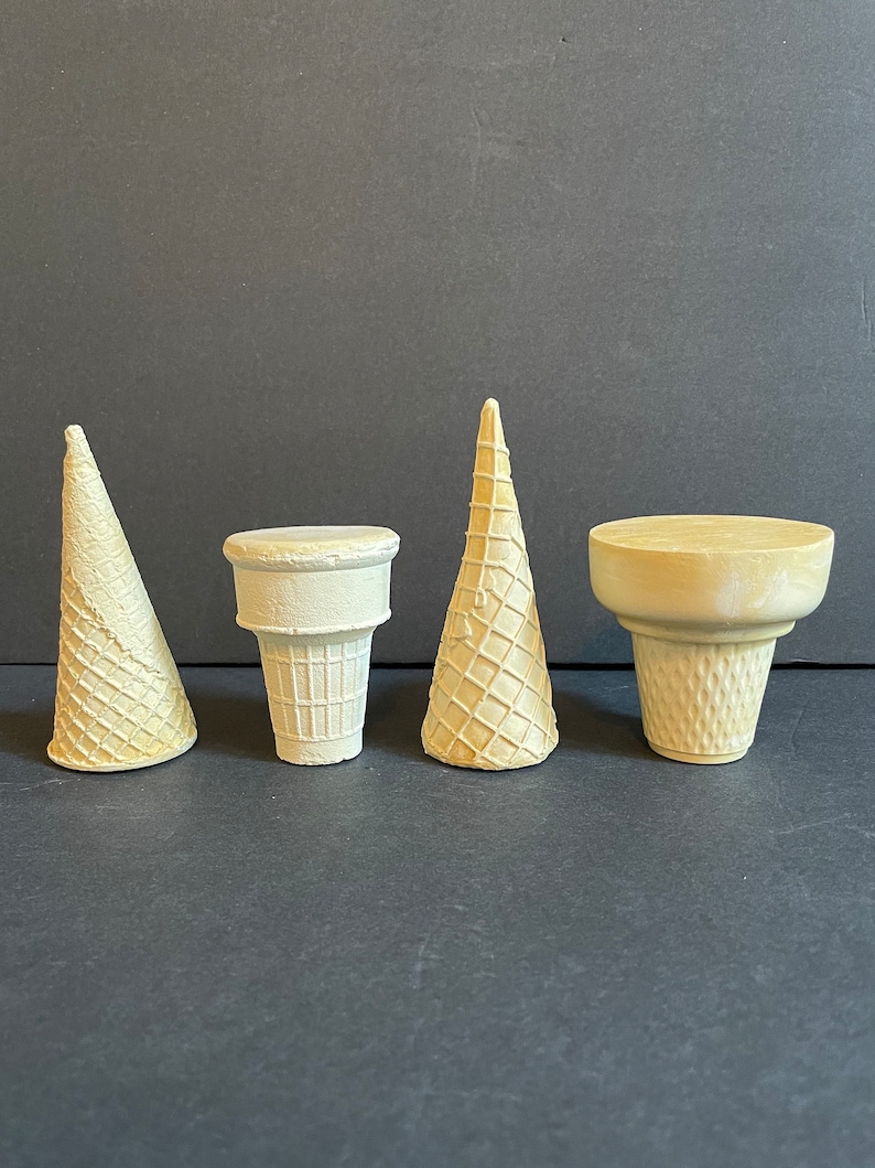 May include: Four white waffle cone ice cream cones, two are upright and two are laying flat. The cones are made of a light brown waffle material.