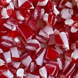 May include: A close-up of red and white candy cane pieces. The candy is broken into small, irregular shapes.