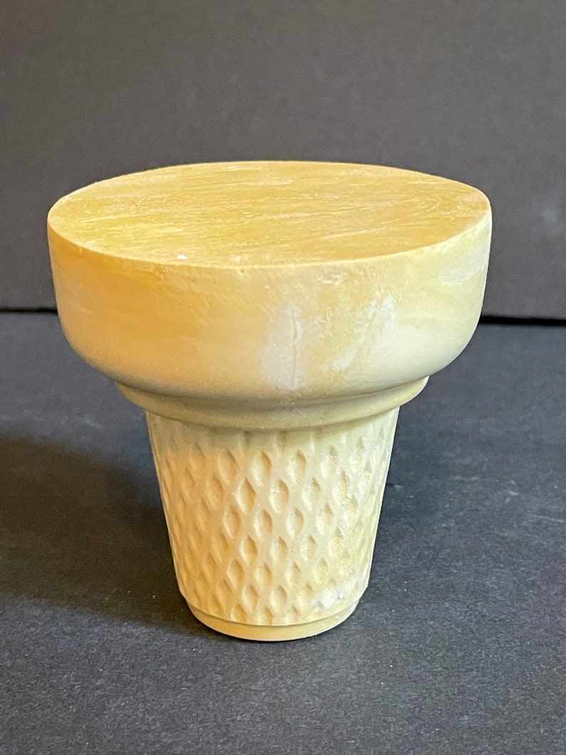 May include: A light beige ceramic ice cream cone mould. The mould is designed to create a realistic ice cream cone shape with a smooth top and a textured waffle cone bottom.