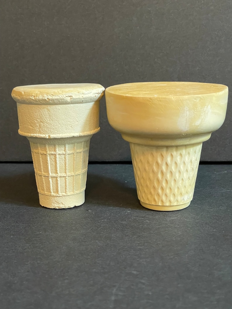 May include: Two empty waffle cone ice cream cones, one is a standard size and the other is a smaller size. Both are made of a light brown paper material.