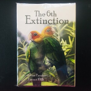 May include: A card with a green and yellow illustration of two Carolina Parakeets, a bird species extinct since 1918. The card has the text "The 6th Extinction" and "Carolina Parakeet Extinct 1918".