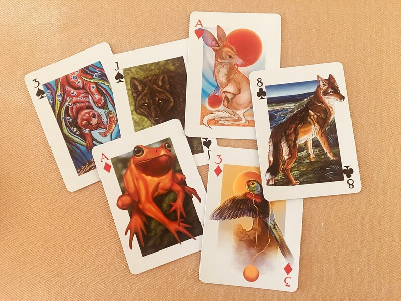May include: A set of playing cards featuring animal illustrations. The cards include the Ace of Diamonds, Jack of Spades, 3 of Spades, 3 of Diamonds, 8 of Clubs, and Ace of Hearts. The cards are arranged in a random order on a brown surface.