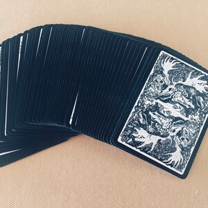 May include: A deck of playing cards with black backs and a white and black illustration of a moose on the face card.