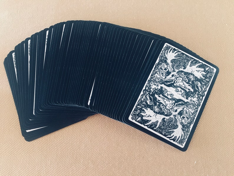 May include: A deck of playing cards with black backs and a white and black illustration of a moose on the face card.