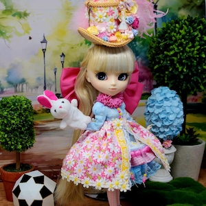 May include: A doll with long blonde hair, wearing a floral hat with feathers and a pink bow. The doll is dressed in a pink and white daisy-patterned dress and holds a white stuffed bunny. The doll's outfit includes a blue top and white boots.