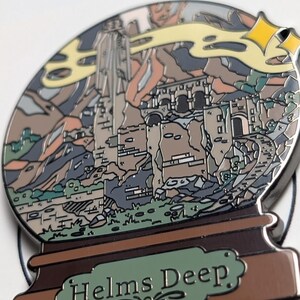 Puede incluir: Un pin de esmalte plateado con forma de bola de nieve con una representaci&oacute;n de Helm's Deep, una fortaleza de la saga de El Se&ntilde;or de los Anillos, en su interior. La base de la bola de nieve es marr&oacute;n con un letrero verde que dice "Helms Deep".