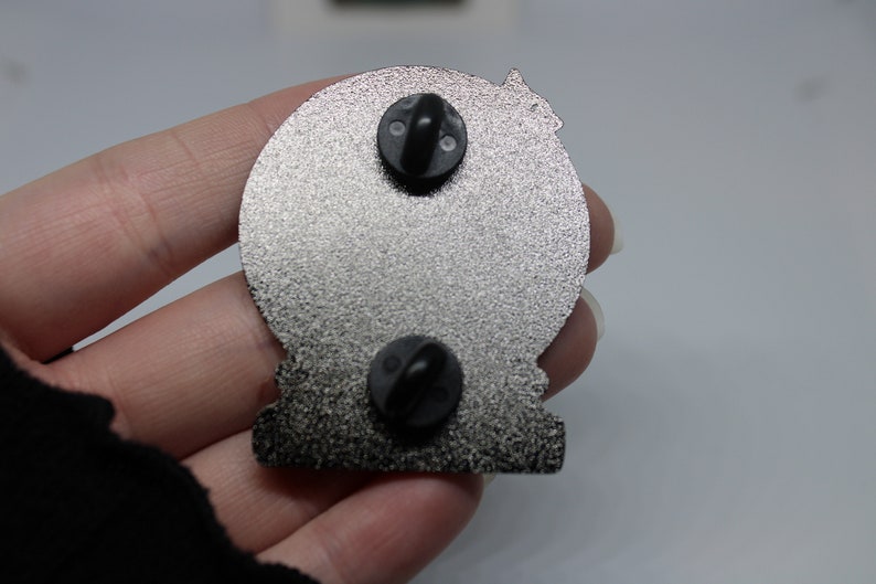 Peut inclure: L'arri&egrave;re d'une &eacute;pingle en m&eacute;tal argent&eacute; avec deux fermoirs papillon noirs. L'&eacute;pingle est en forme de cercle avec une surface textur&eacute;e.