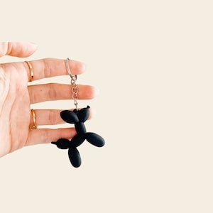 May include: Black balloon animal keychain shaped like a dog. The keychain is attached to a silver metal chain.