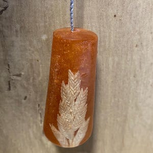 May include: An amber-coloured resin pull with a silver cord. The pull features a detailed, light-coloured wheat design embedded within the resin. The pull is cylindrical and appears to be suspended.