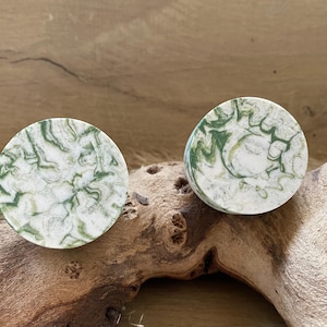 May include: A pair of round, green and white marbled coasters. The coasters have a swirling pattern of green and white.