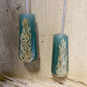May include: Two green resin light pulls with a wheat design. Each pull is cylindrical and features a golden wheat stalk encased within the translucent green resin. The pulls are suspended by a silver cord, ideal for a bathroom or bedroom.