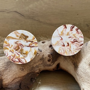 May include: Two round, white resin earrings with a marbled pattern in shades of brown, red, and gold.