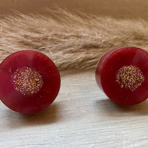May include: Two round red resin earrings with a gold glitter centre.