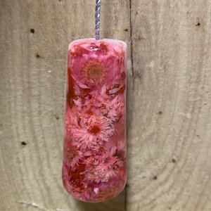 May include: A cylindrical, pink and red floral resin pull with a silver cord. The resin is filled with dried flowers, creating a decorative design. The pull is likely for a light fixture or similar.