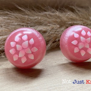 May include: Two pink round knobs with a white floral design. The knobs are made of resin and have a glossy finish.