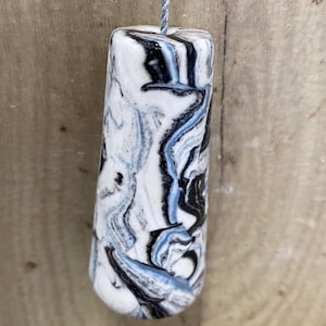 May include: A cylindrical light pull with a marbled design. The pull has a white base with swirling patterns in black and light blue. A light blue cord is attached to the top of the pull.