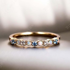 May include: A delicate gold band ring with a row of alternating opal and blue gemstones. The ring is set with small, round stones.